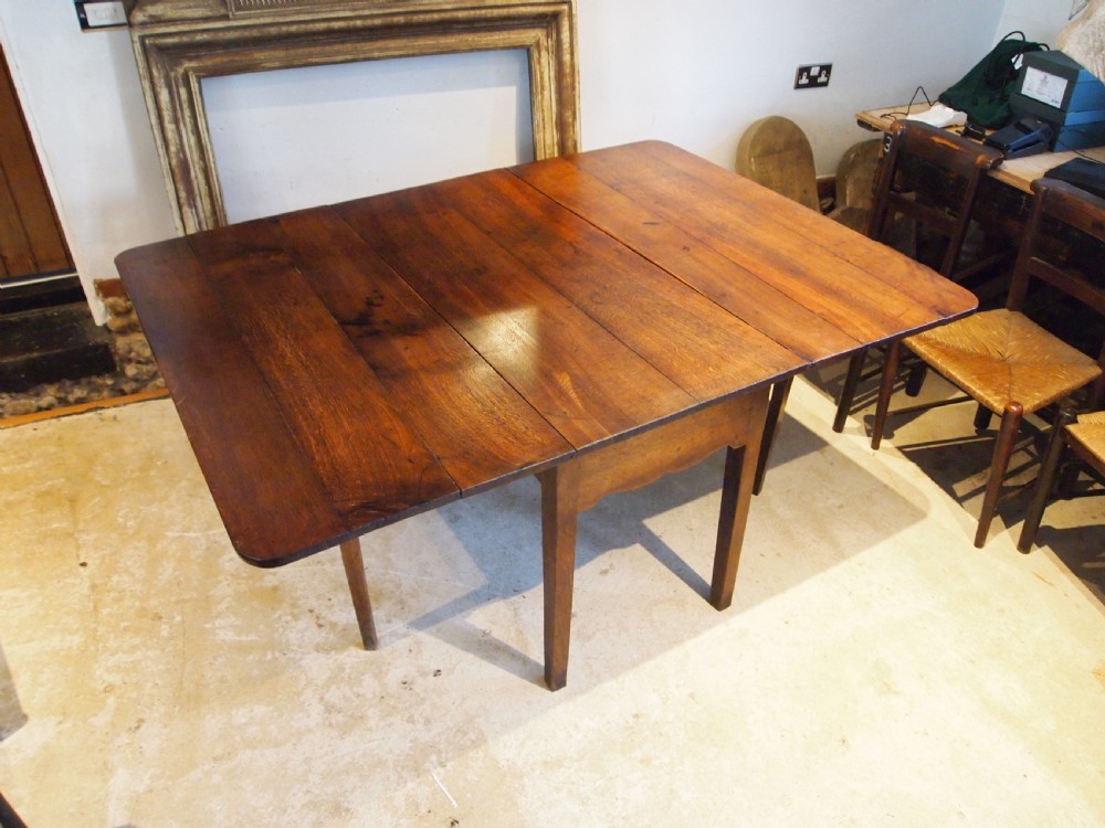 An 18th-century George III Welsh oak drop-leaf dining table with square tapered legs and a shaped apron.