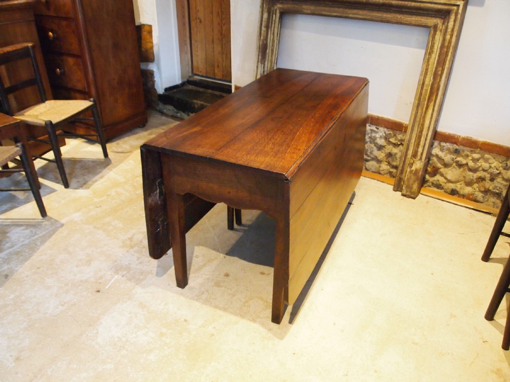 An 18th-century George III Welsh oak drop-leaf dining table with square tapered legs and a shaped apron. View II