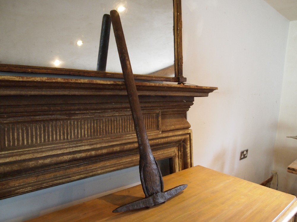 An antique nineteenth-century miners pickaxe with a dark turned wooden handle and a hand-forged iron head.