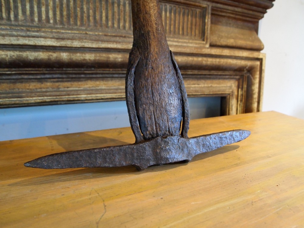 An antique nineteenth-century miners pickaxe with a dark turned wooden handle and a hand-forged iron head. View II