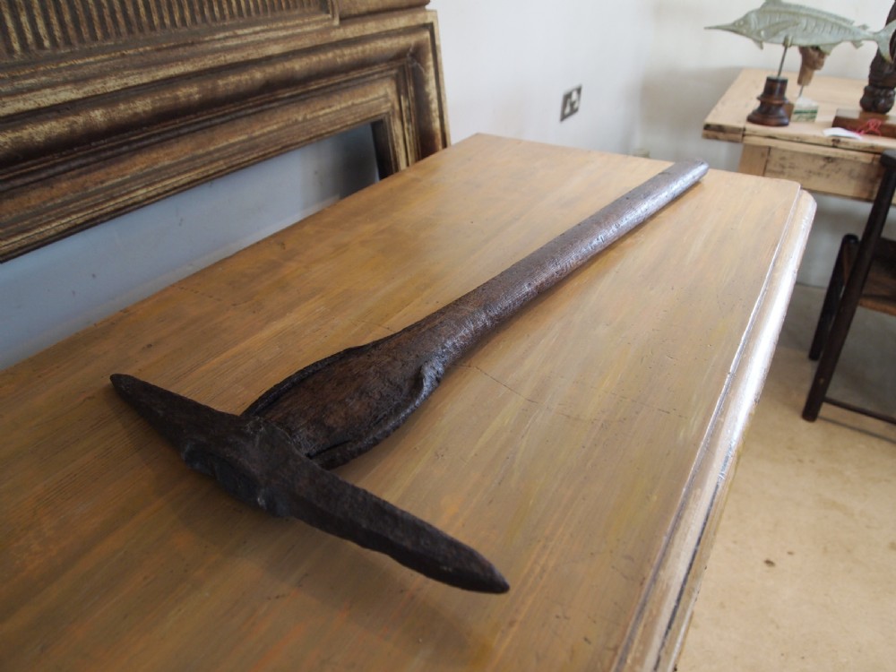An antique nineteenth-century miners pickaxe with a dark turned wooden handle and a hand-forged iron head. View X