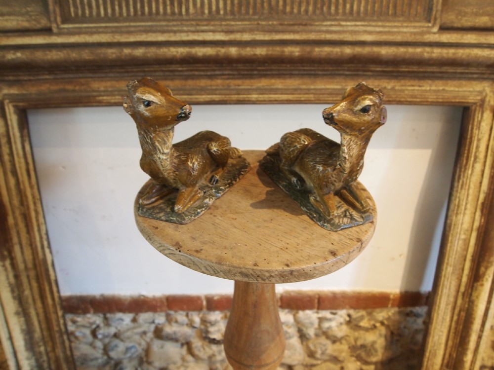 A pair of hand-carved limewood fawns in recumbent poses with detailed carved fur on integral wooden bases.
