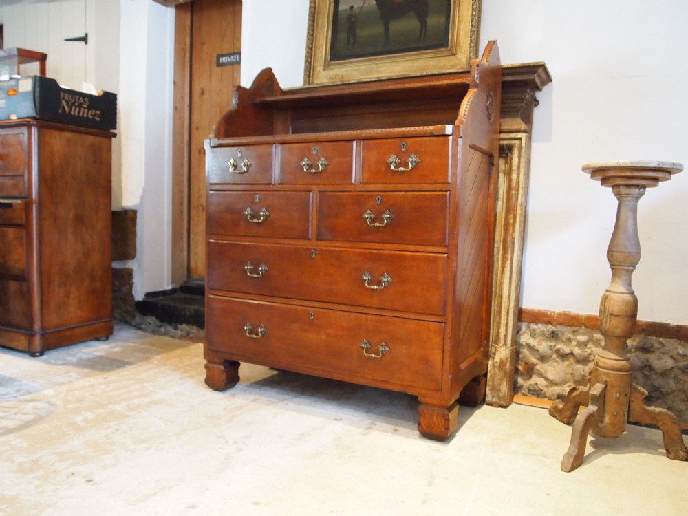 A Victorian oak chest of drawers featuring an upper gallery shelf, seven drawers with ornate brass drop handles, and planked sides.