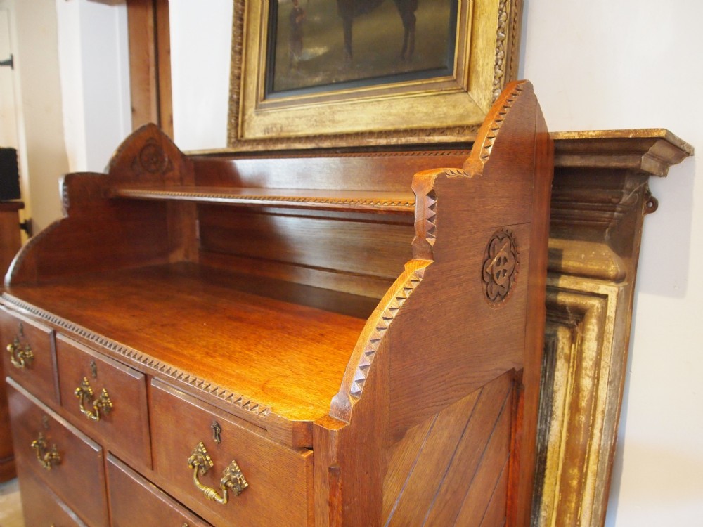 A Victorian oak chest of drawers featuring an upper gallery shelf, seven drawers with ornate brass drop handles, and planked sides. View III