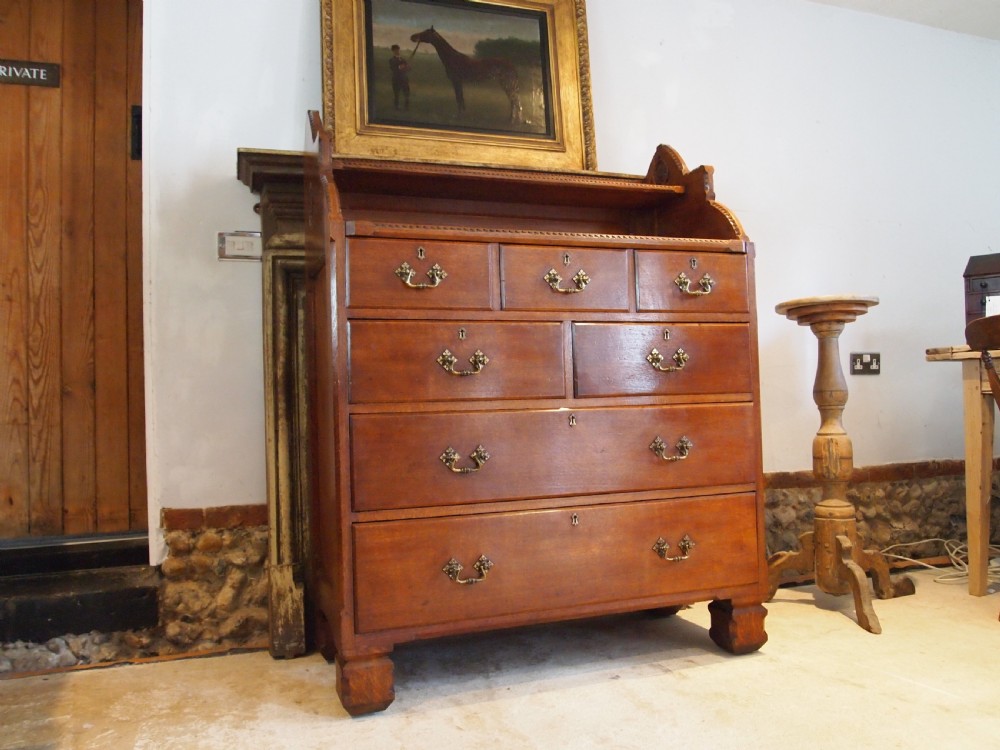 A Victorian oak chest of drawers featuring an upper gallery shelf, seven drawers with ornate brass drop handles, and planked sides. View V