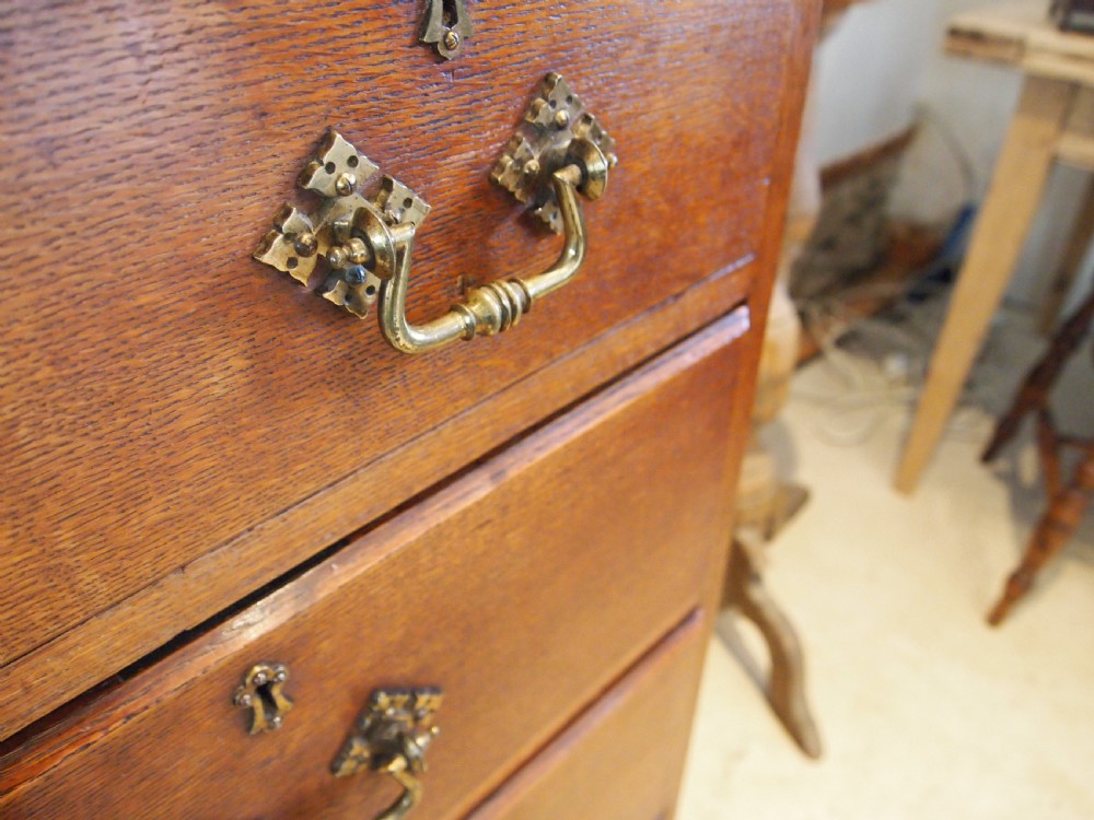 A Victorian oak chest of drawers featuring an upper gallery shelf, seven drawers with ornate brass drop handles, and planked sides. View VIII