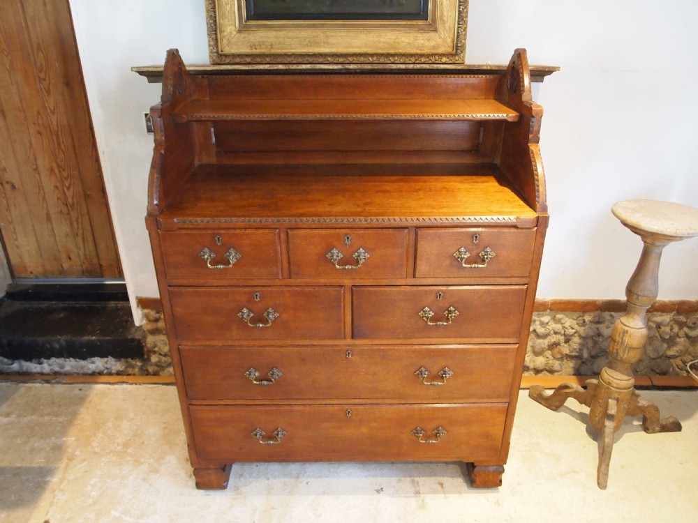 A Victorian oak chest of drawers featuring an upper gallery shelf, seven drawers with ornate brass drop handles, and planked sides. View X