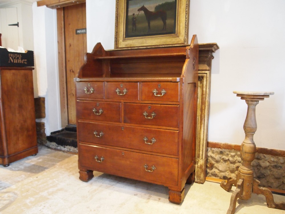 A Victorian oak chest of drawers featuring an upper gallery shelf, seven drawers with ornate brass drop handles, and planked sides. View XI
