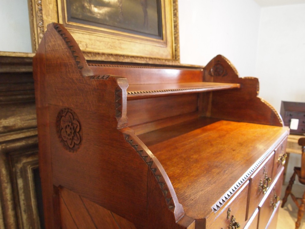 A Victorian oak chest of drawers featuring an upper gallery shelf, seven drawers with ornate brass drop handles, and planked sides. View XIII