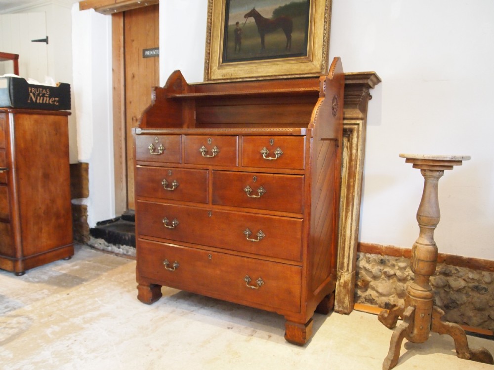 A Victorian oak chest of drawers featuring an upper gallery shelf, seven drawers with ornate brass drop handles, and planked sides. View XIV
