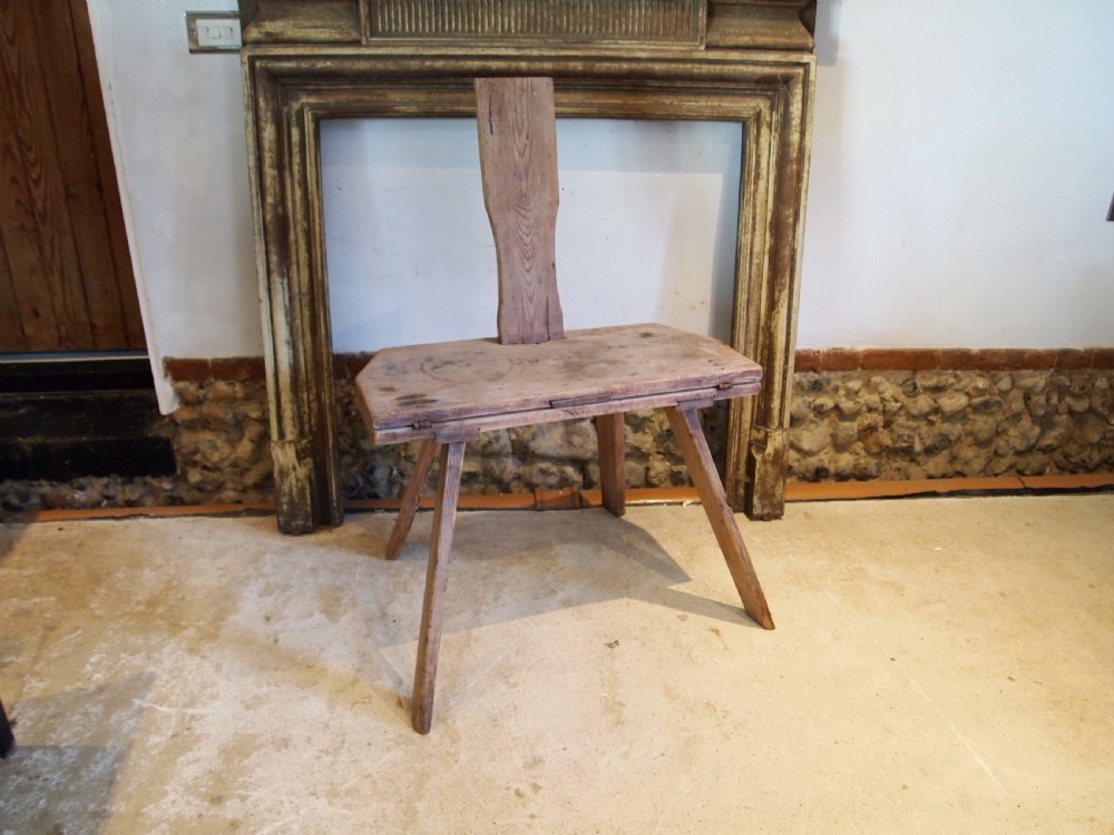 A George III primitive pine chair table featuring a tall central wooden backboard splat, flat bench seat, iron hinges, and four splayed round legs.