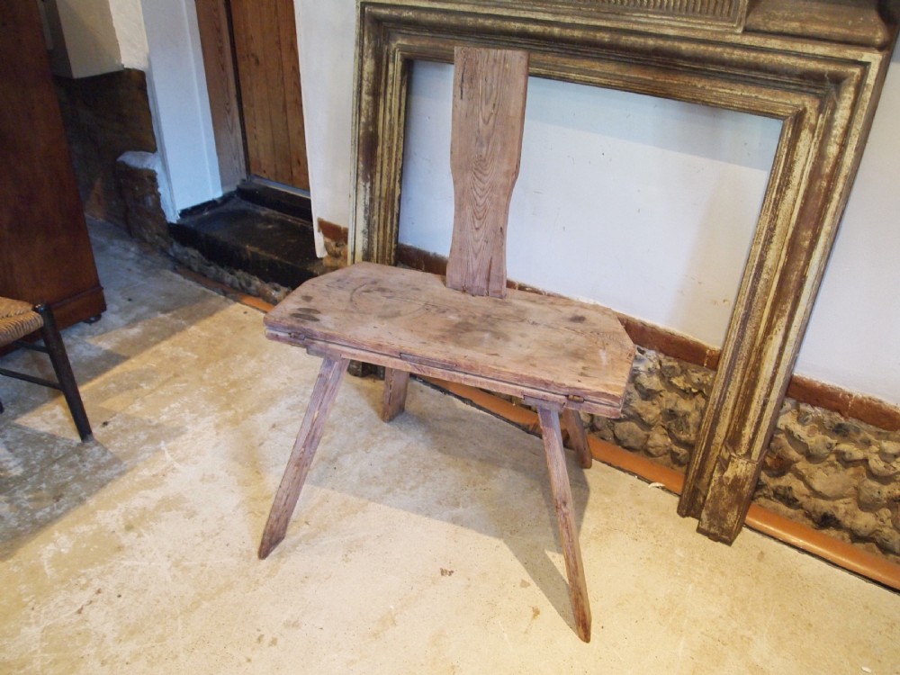 A George III primitive pine chair table featuring a tall central wooden backboard splat, flat bench seat, iron hinges, and four splayed round legs. View III