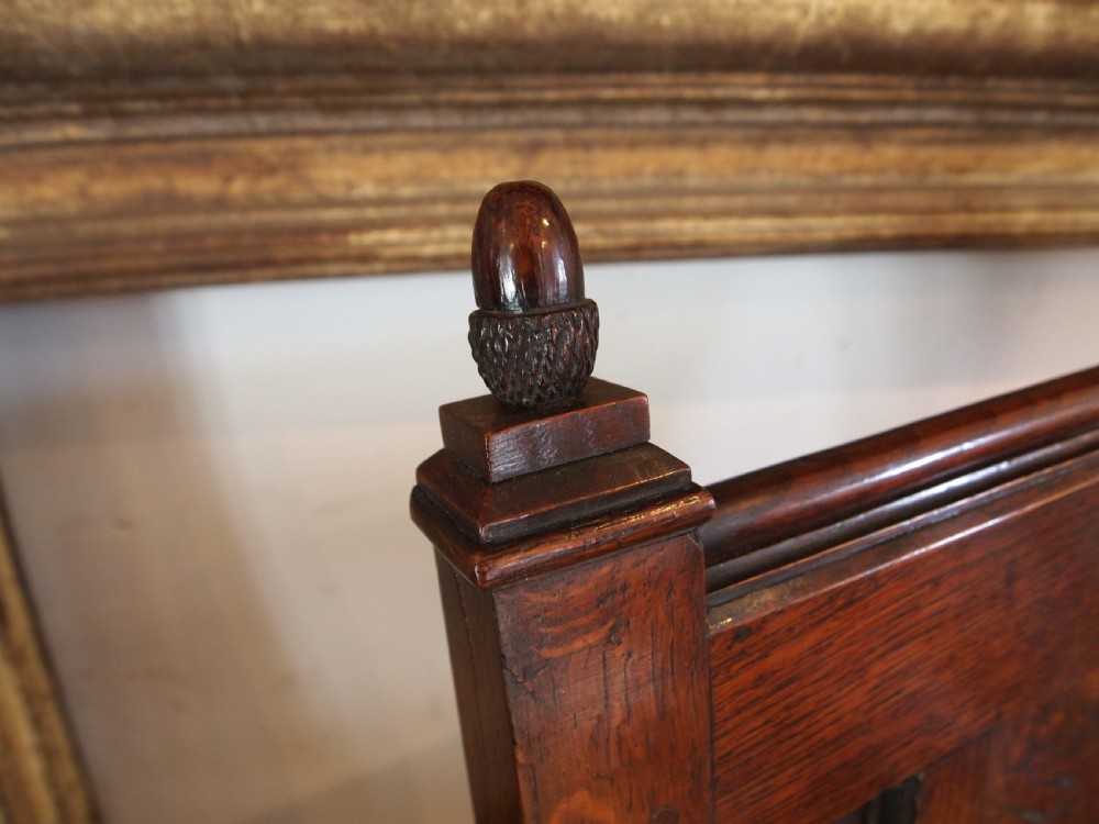An eighteenth-century dark oak wainscot armchair featuring a panelled backrest, carved finials, turned front legs, and sturdy wooden stretchers. View II