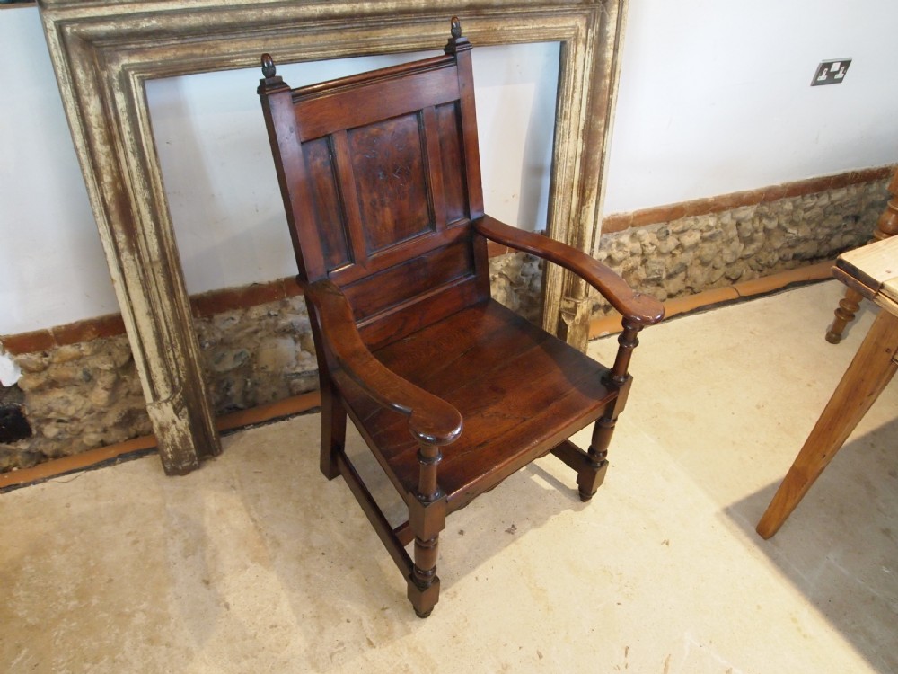 An eighteenth-century dark oak wainscot armchair featuring a panelled backrest, carved finials, turned front legs, and sturdy wooden stretchers. View V
