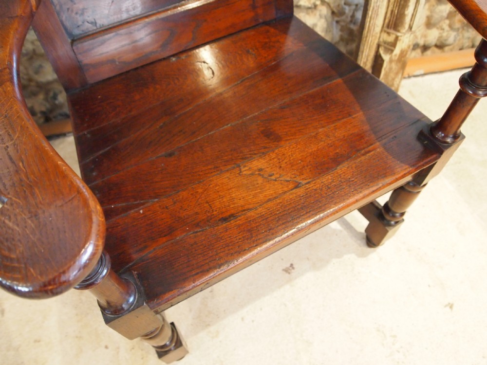 An eighteenth-century dark oak wainscot armchair featuring a panelled backrest, carved finials, turned front legs, and sturdy wooden stretchers. View XI