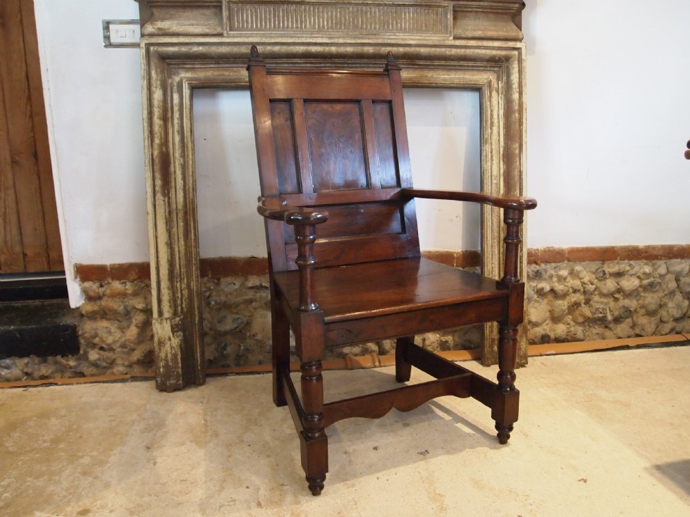 An eighteenth-century dark oak wainscot armchair featuring a panelled backrest, carved finials, turned front legs, and sturdy wooden stretchers. View XIII