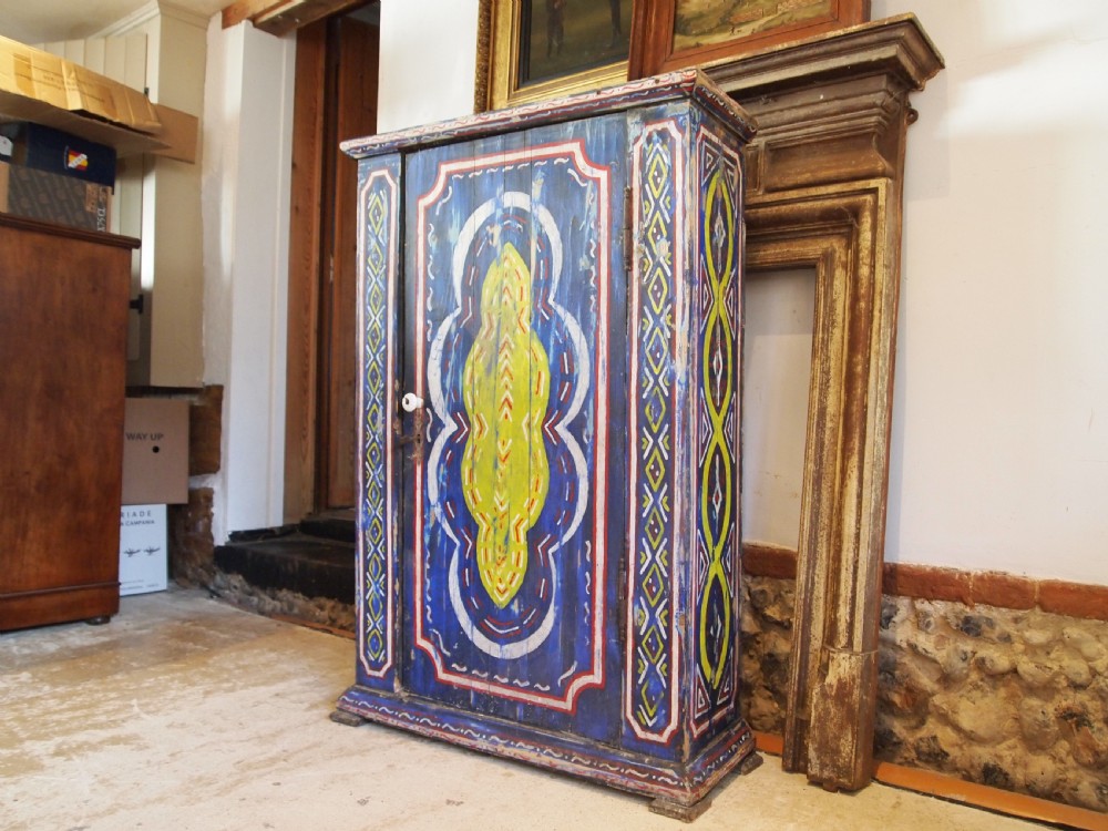 A Victorian pine single-door cupboard decorated with vibrant hand-painted blue, yellow, red, and white geometric folk art motifs.