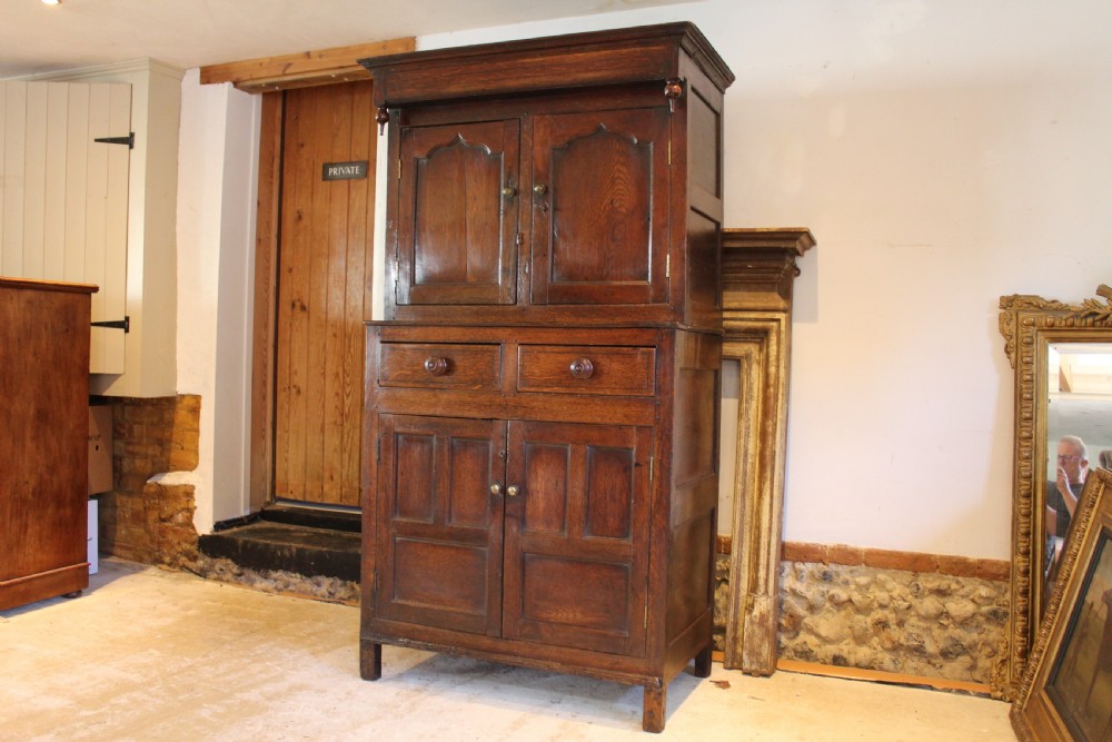 An 18th-century dark oak Welsh Cwpwrdd Deuddarn featuring a two-stage cupboard design with arched panelled upper doors, pendant drop finials, and lower drawers. View II