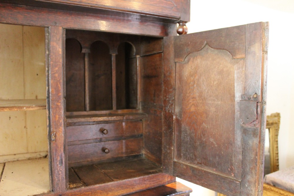 An 18th-century dark oak Welsh Cwpwrdd Deuddarn featuring a two-stage cupboard design with arched panelled upper doors, pendant drop finials, and lower drawers. View VI