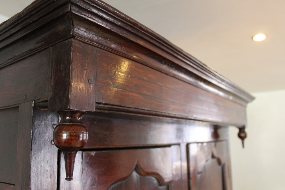 An 18th-century dark oak Welsh Cwpwrdd Deuddarn featuring a two-stage cupboard design with arched panelled upper doors, pendant drop finials, and lower drawers. View VII