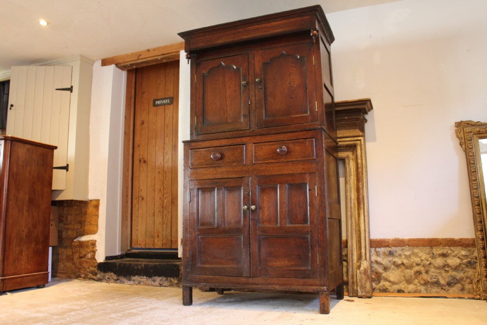 An 18th-century dark oak Welsh Cwpwrdd Deuddarn featuring a two-stage cupboard design with arched panelled upper doors, pendant drop finials, and lower drawers. View XI