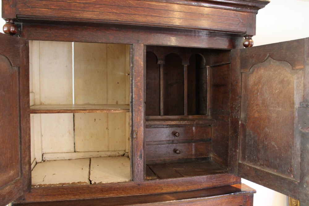An 18th-century dark oak Welsh Cwpwrdd Deuddarn featuring a two-stage cupboard design with arched panelled upper doors, pendant drop finials, and lower drawers. View XII
