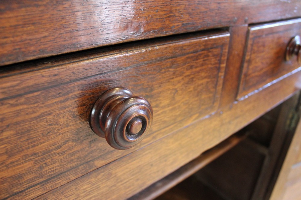 An 18th-century dark oak Welsh Cwpwrdd Deuddarn featuring a two-stage cupboard design with arched panelled upper doors, pendant drop finials, and lower drawers. View XVI