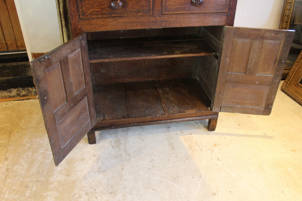 An 18th-century dark oak Welsh Cwpwrdd Deuddarn featuring a two-stage cupboard design with arched panelled upper doors, pendant drop finials, and lower drawers. View XVII