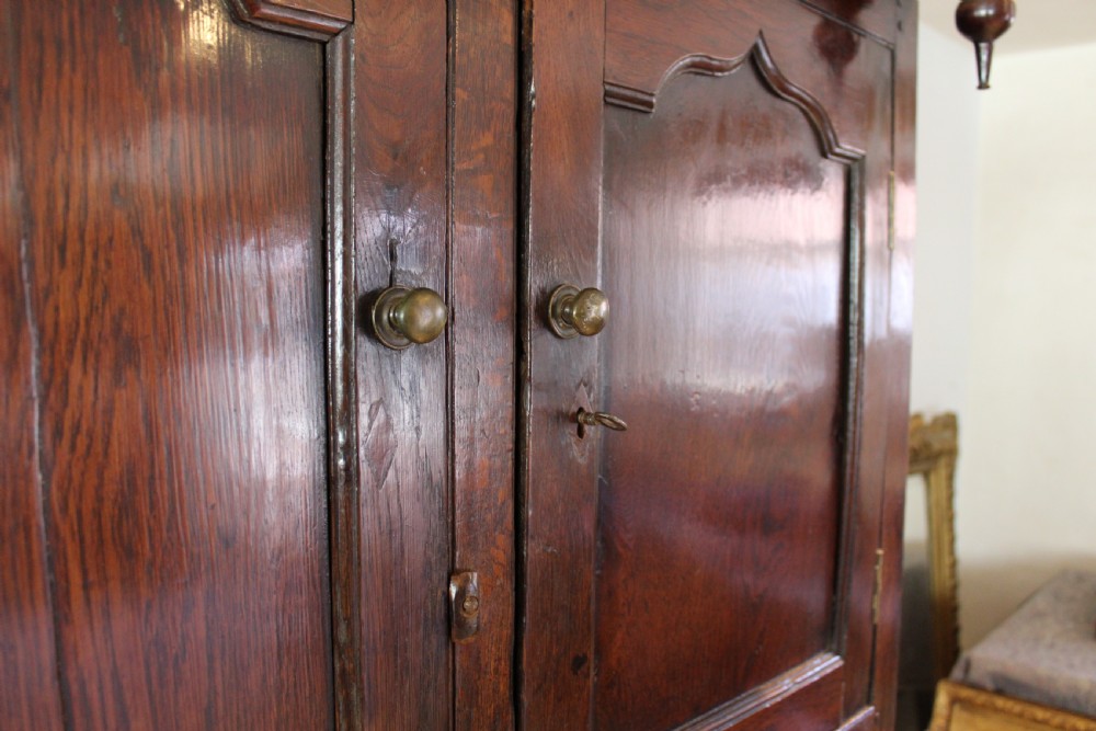 An 18th-century dark oak Welsh Cwpwrdd Deuddarn featuring a two-stage cupboard design with arched panelled upper doors, pendant drop finials, and lower drawers. View XIX