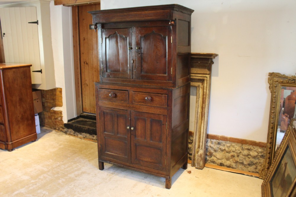 An 18th-century dark oak Welsh Cwpwrdd Deuddarn featuring a two-stage cupboard design with arched panelled upper doors, pendant drop finials, and lower drawers. View XX