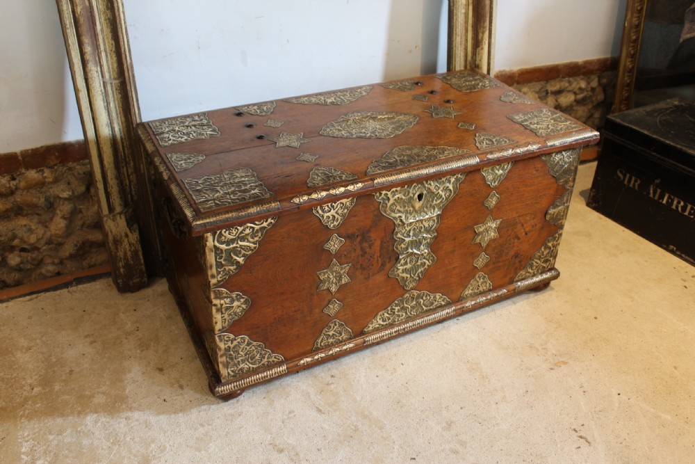 An antique warm brown teak wooden chest adorned with elaborate pierced brass plates, star-shaped metal appliques, and brass stud detailing.