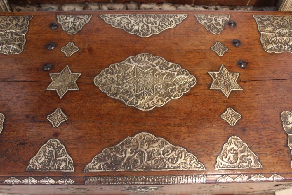 An antique warm brown teak wooden chest adorned with elaborate pierced brass plates, star-shaped metal appliques, and brass stud detailing. View II