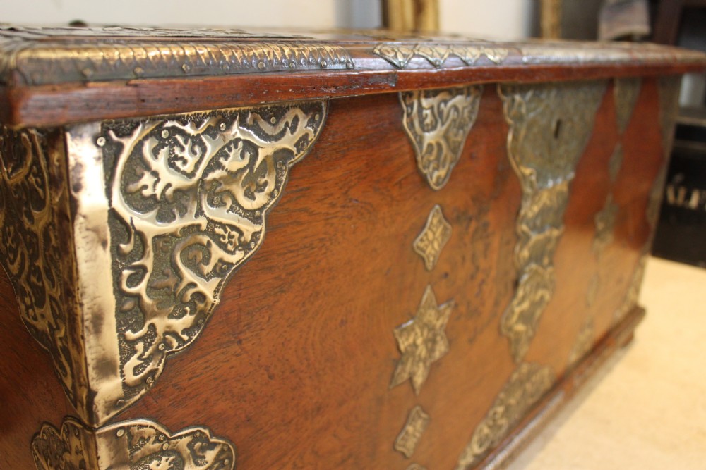 An antique warm brown teak wooden chest adorned with elaborate pierced brass plates, star-shaped metal appliques, and brass stud detailing. View VI