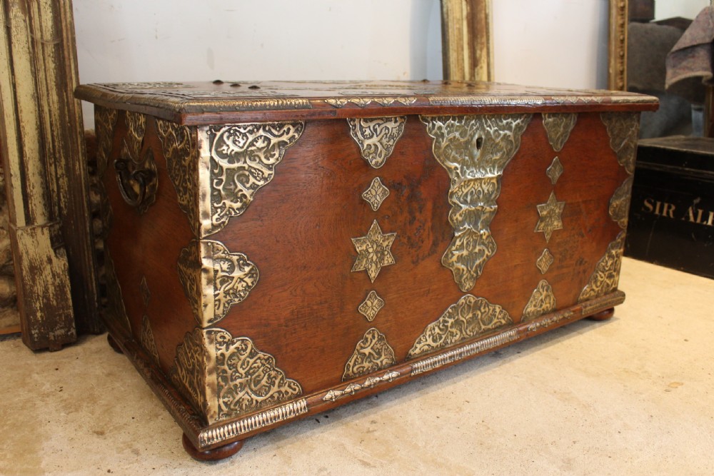 An antique warm brown teak wooden chest adorned with elaborate pierced brass plates, star-shaped metal appliques, and brass stud detailing. View XIV