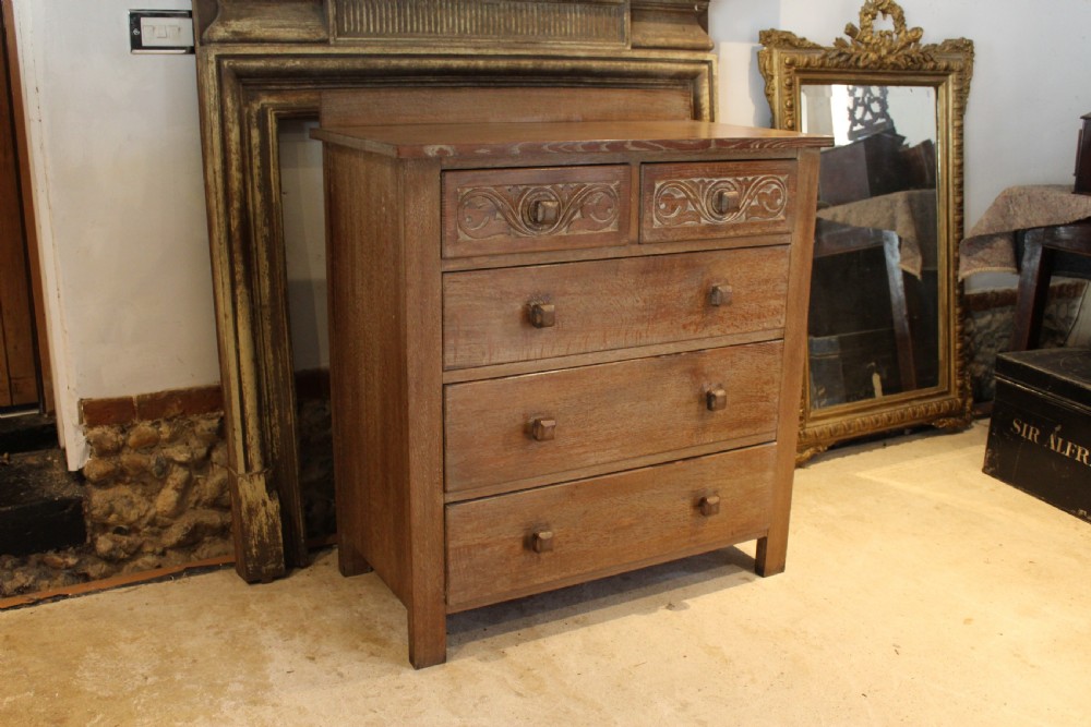 An Arts and Crafts limed oak chest of drawers featuring two upper drawers with stylised carved relief patterns and three long drawers below with square wooden handles. View II