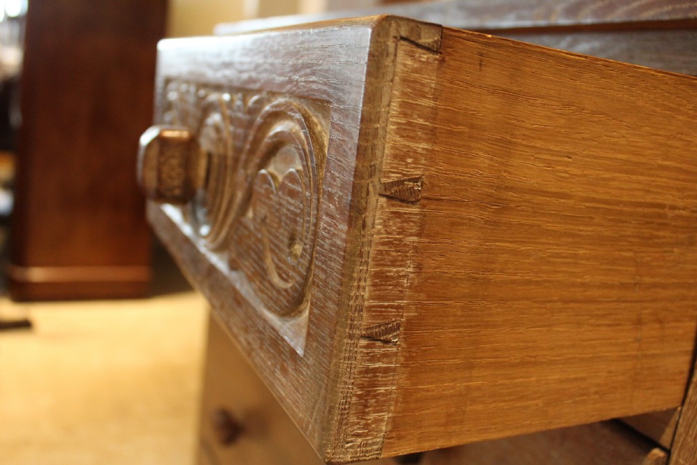 An Arts and Crafts limed oak chest of drawers featuring two upper drawers with stylised carved relief patterns and three long drawers below with square wooden handles. View III