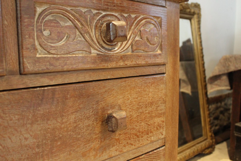 An Arts and Crafts limed oak chest of drawers featuring two upper drawers with stylised carved relief patterns and three long drawers below with square wooden handles. View VI