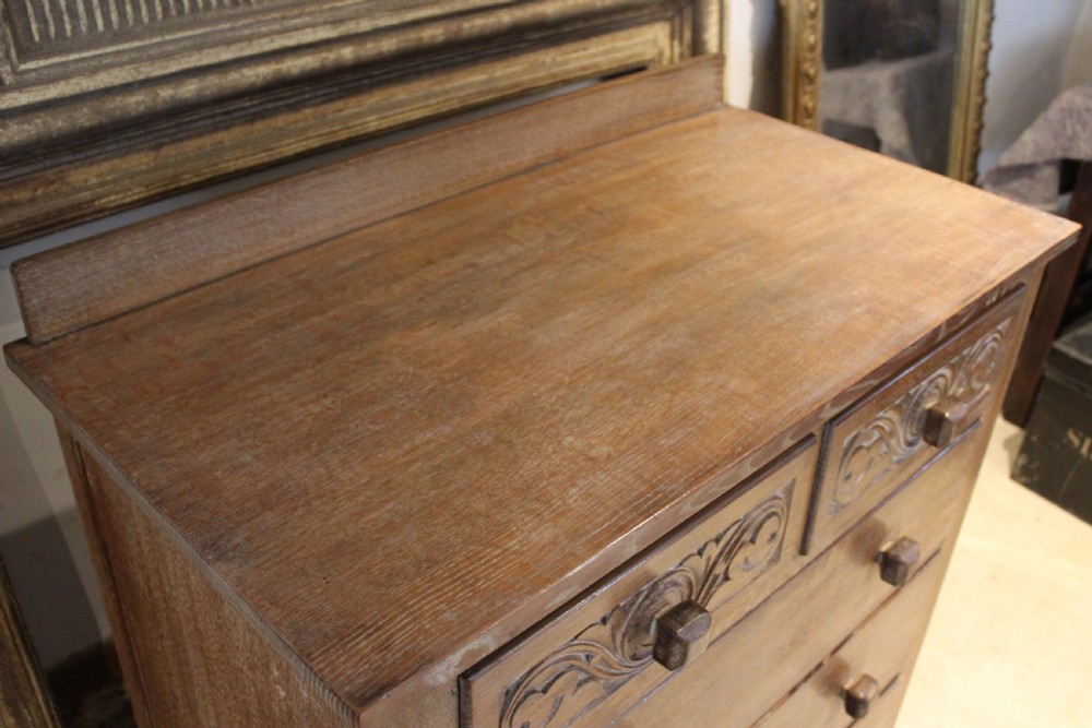 An Arts and Crafts limed oak chest of drawers featuring two upper drawers with stylised carved relief patterns and three long drawers below with square wooden handles. View VIII