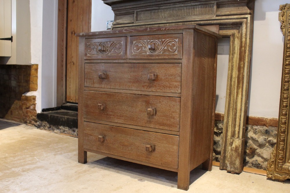 An Arts and Crafts limed oak chest of drawers featuring two upper drawers with stylised carved relief patterns and three long drawers below with square wooden handles. View X
