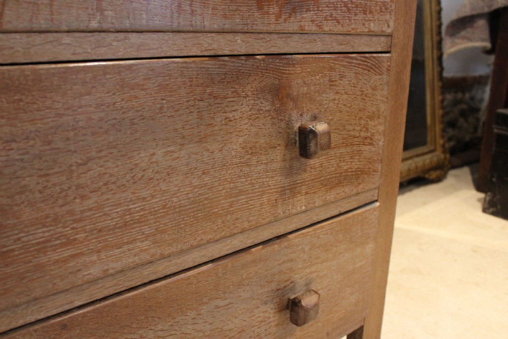 An Arts and Crafts limed oak chest of drawers featuring two upper drawers with stylised carved relief patterns and three long drawers below with square wooden handles. View XI