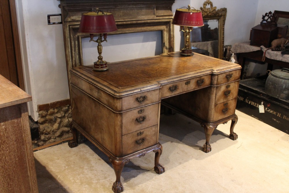 An early twentieth-century Queen Anne style burr walnut pedestal desk featuring carved cabriole legs with claw and ball feet, brass handles, and a leather writing surface.