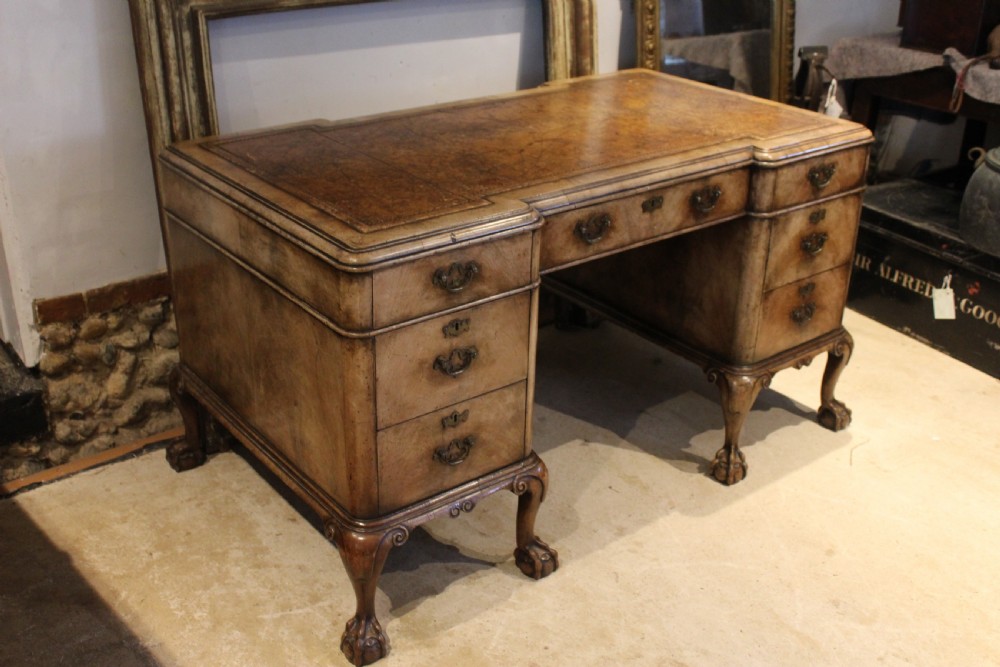 An early twentieth-century Queen Anne style burr walnut pedestal desk featuring carved cabriole legs with claw and ball feet, brass handles, and a leather writing surface. View II