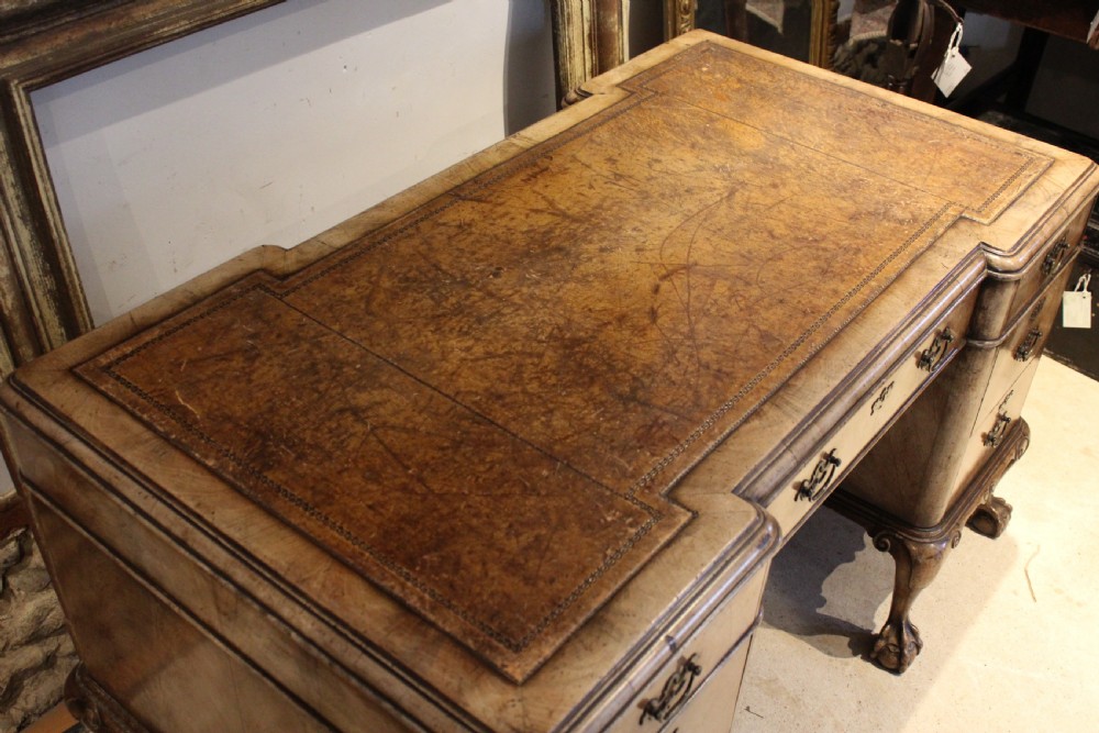An early twentieth-century Queen Anne style burr walnut pedestal desk featuring carved cabriole legs with claw and ball feet, brass handles, and a leather writing surface. View X