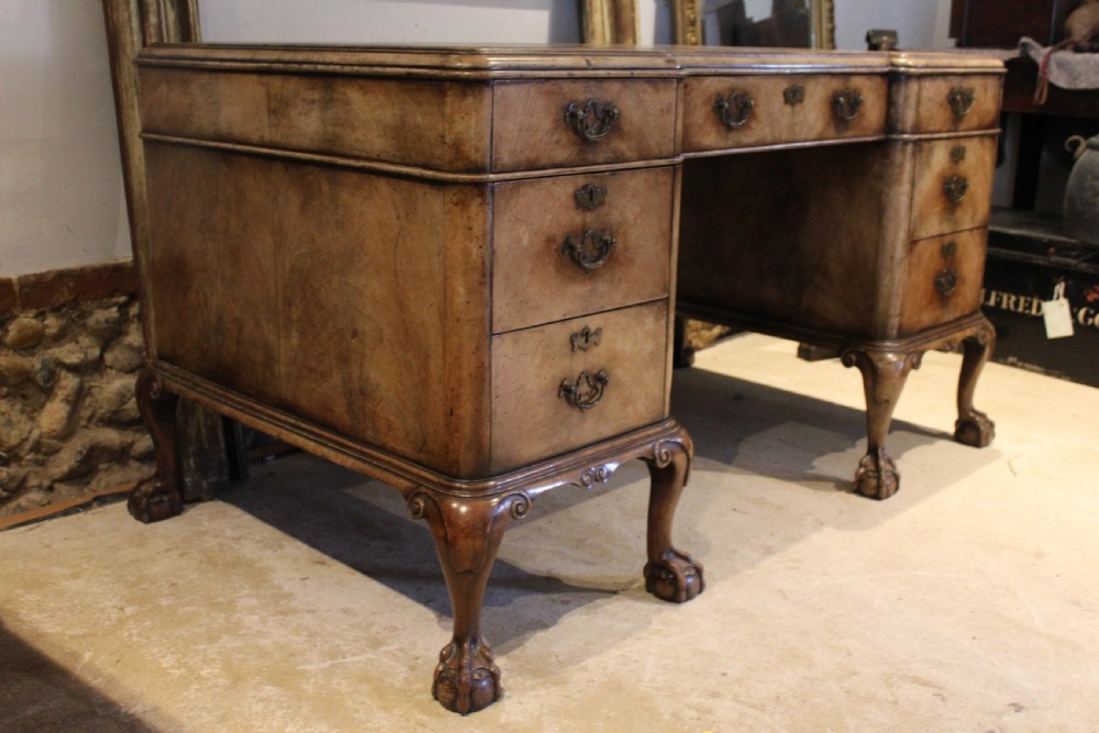 An early twentieth-century Queen Anne style burr walnut pedestal desk featuring carved cabriole legs with claw and ball feet, brass handles, and a leather writing surface. View XVI