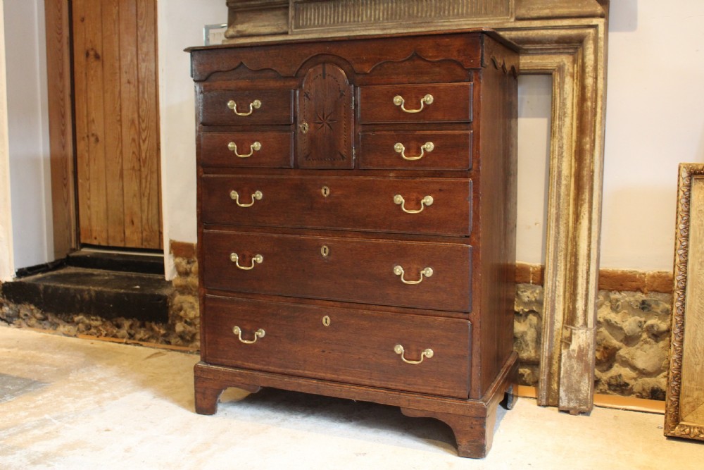 An 18th-century Georgian oak chest of drawers featuring brass swan-neck handles, a central carved arch door, and bracket feet.