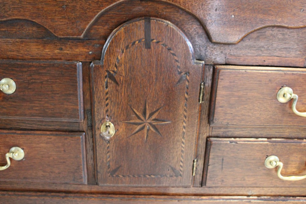 An 18th-century Georgian oak chest of drawers featuring brass swan-neck handles, a central carved arch door, and bracket feet. View II