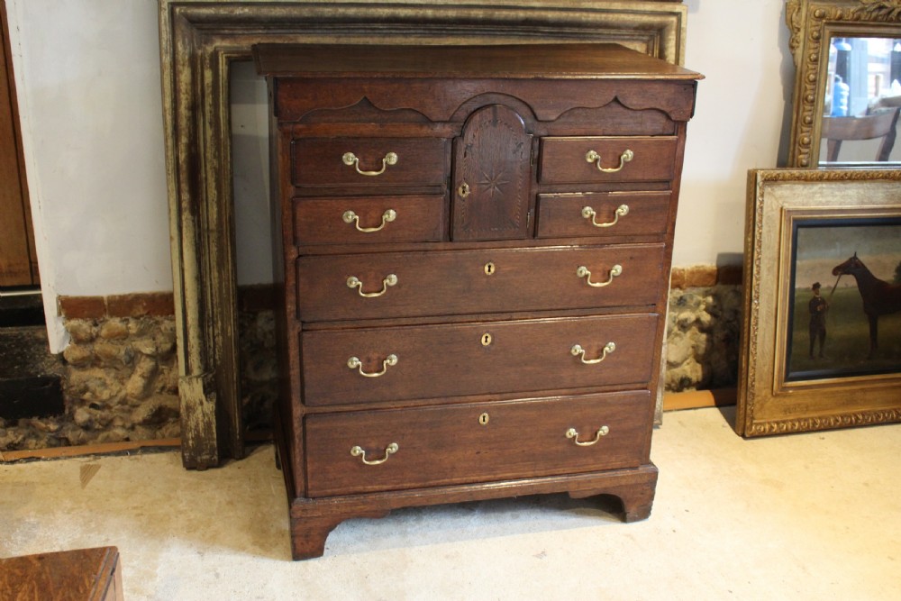 An 18th-century Georgian oak chest of drawers featuring brass swan-neck handles, a central carved arch door, and bracket feet. View III