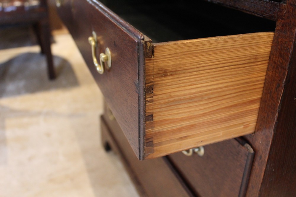 An 18th-century Georgian oak chest of drawers featuring brass swan-neck handles, a central carved arch door, and bracket feet. View XI