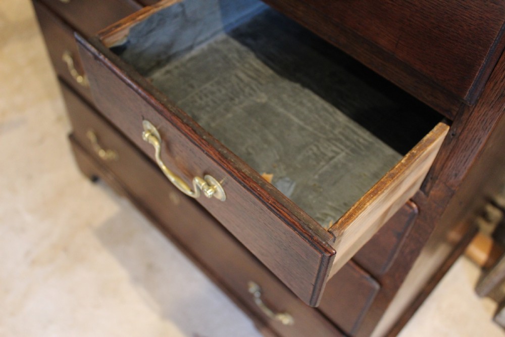 An 18th-century Georgian oak chest of drawers featuring brass swan-neck handles, a central carved arch door, and bracket feet. View XII