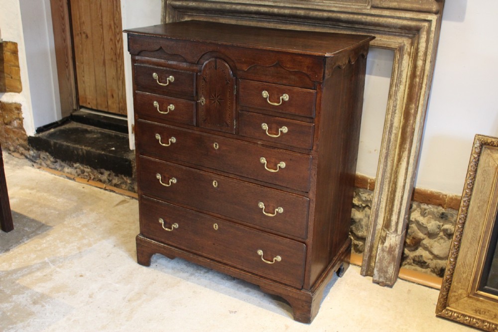 An 18th-century Georgian oak chest of drawers featuring brass swan-neck handles, a central carved arch door, and bracket feet. View XIII